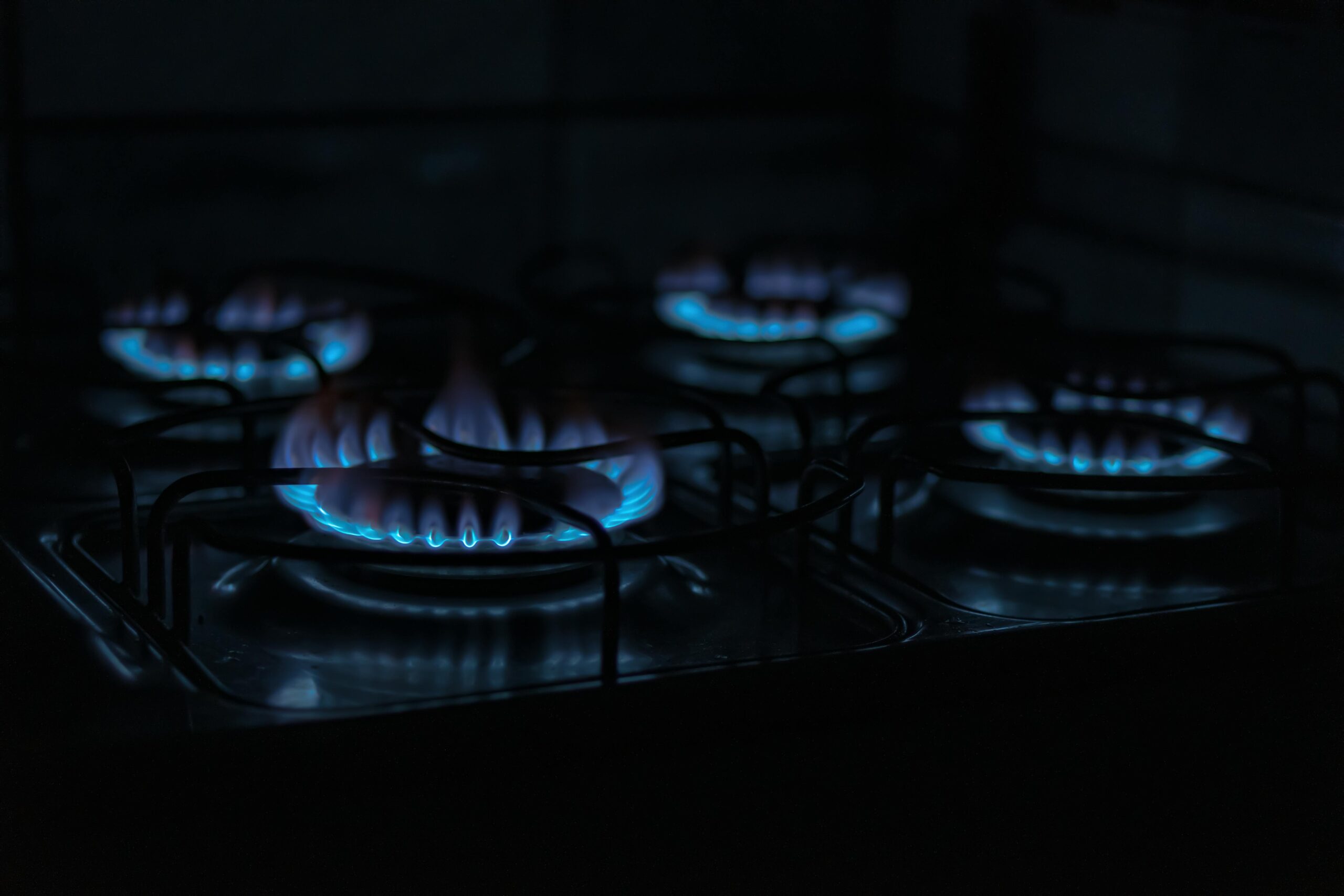 pexels-photo-4063198-4063198 A dark, atmospheric image capturing the blue flames of gas stove burners indoors.